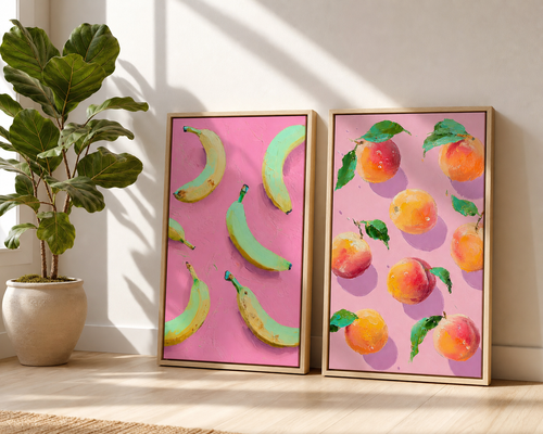 Two framed artworks with banana and peach patterns on a pink background, placed on a wooden floor with a plant beside them.